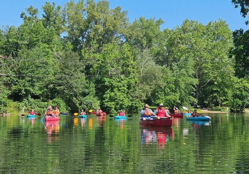 Kayakers enjoying a sunny day on Blackstone River. Surrounded by lush green trees. Perfect outdoor activity.